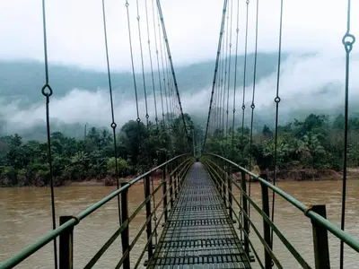 a suspension bridge over a river in the jungle at Holy Village Homestay in Neriyamangalam