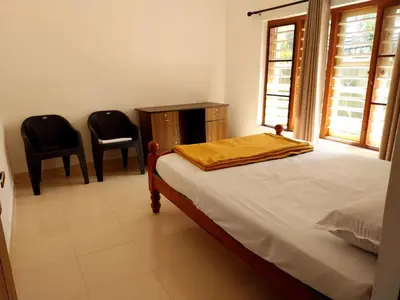 a bedroom with a bed with two chairs and a window at Nature's View Service Villa in Vythiri