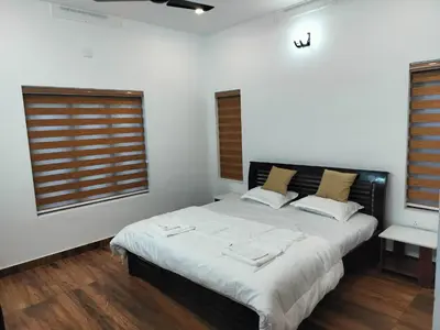 a bedroom with a large bed and two windows at Roneys Villa in Wayanad