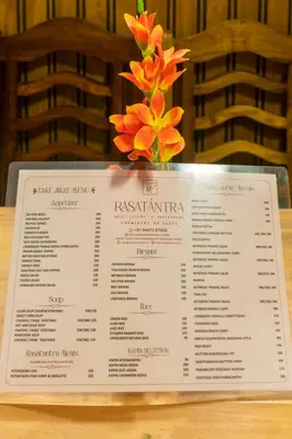 a menu on a table with a vase of flowers at Base9 Family Lounge -Cochin Airport in Nedumbassery