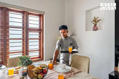 a man standing in a kitchen with a tray of orange juice at Stayvista at Whitewood Serene 5BHK Homestay - Wayanad in Wayanad
