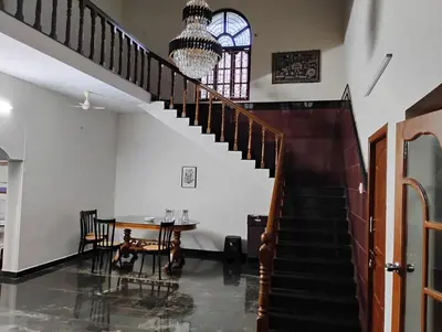 a staircase in a house with a table and a chandelier at Vasantham Home Stay in Satyamangalam