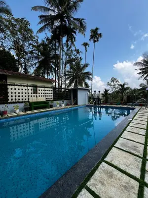 a pool at a hotel with palm trees in the background at Wild mist in Padinjarathara
