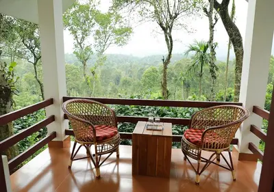 a balcony with two chairs and a table with a view at Dhanagiri Homestay Wayanad in Vythiri