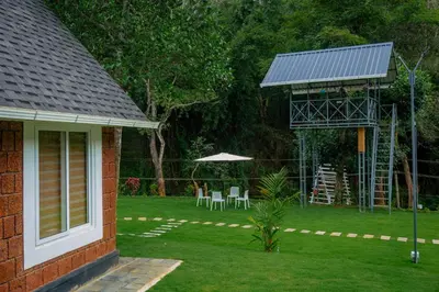 a house with a yard with chairs and an umbrella at Misty Forest Resort Wayanad in Wayanad