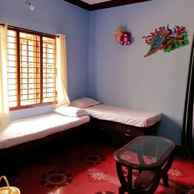 a room with two beds and a table and a window at Aghasthyashrya Homestay in Siddapur