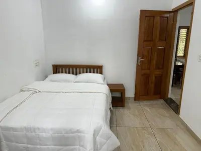 a bedroom with a bed with white sheets and a wooden door at Serenity Home Stay in Sultan Bathery
