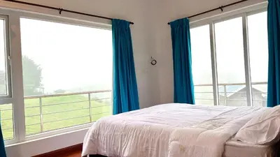 a bedroom with a bed and two large windows at Away From Home - 6 - Rooms In Ooty, Home Stay Ooty in Ooty