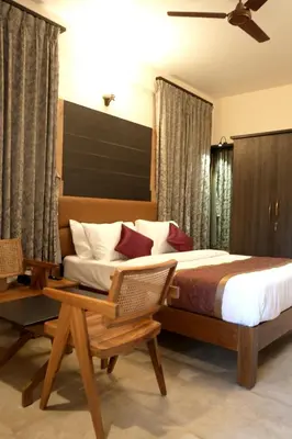 a bedroom with a bed and a chair and a table at Hotel Orchard Coorg in Virajpet