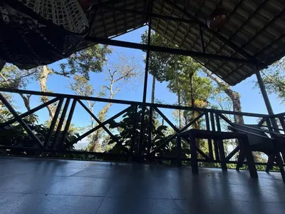 a porch with a bench and trees in the background at The Cozy Clouds Hill Saty in Madikeri
