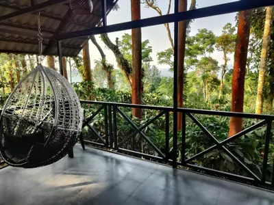 a hammock hanging from a porch with a view of trees at The Cozy Clouds Hill Saty in Madikeri