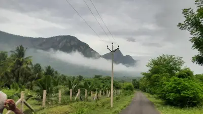 a road with a mountain in the background with clouds at Yes Yes Farms in Pollāchi