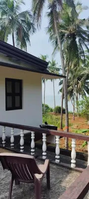 a house with a bench on a balcony with palm trees at Casa Shanti in Kannur