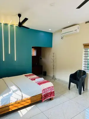 a bedroom with a large bed and a black chair at Jungle Farm House in Kollengode