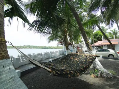 a hammock hanging from two palm trees next to the water at karimeen hut in Irimbranallūr