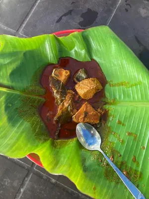 a plate of food on a green leaf with a spoon at karimeen hut in Irimbranallūr