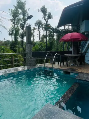 a swimming pool with a table and an umbrella at Coorg Sana Riverside in Suntikoppa