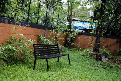 a black bench sitting in the grass next to a fence at sky blue villa in Vythiri