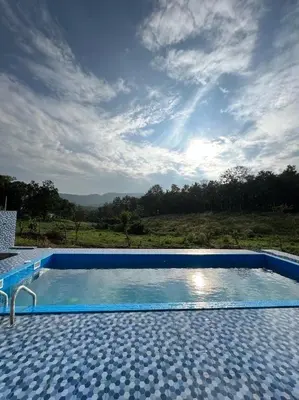 a blue swimming pool with a cloudy sky at Wildglamps Athirappilly in Athirappilly