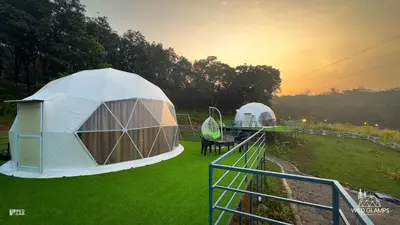 two tents on a grass field with the sunset at Wildglamps Athirappilly in Athirappilly