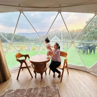 a woman holding a child at a table in front of a window at Wildglamps Athirappilly in Athirappilly