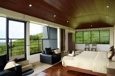 a bedroom with a bed and a chair and windows at Ibex Resorts, Valparai Tale Rock in Vālpārai