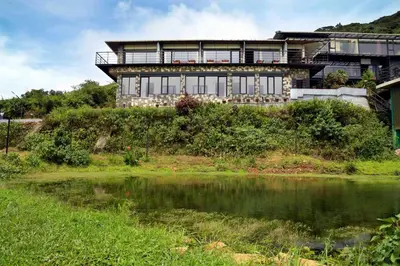 a house on top of a hill next to a body of water at Ibex Resorts, Valparai Tale Rock in Vālpārai