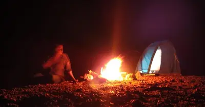 a person sitting next to a fire in front of a tent at Gypsy habitat Backpackers Space in Wodapatti