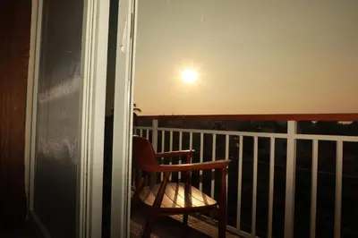 a chair sitting on a balcony with the sun in the sky at Nilgiri Woodlands Luxury Service Apartments in Mysore