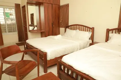 two beds in a room with a chair and a chair at Nilgiri Woodlands Luxury Service Apartments in Mysore