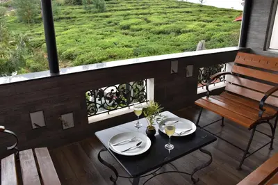 a table with two wine glasses and a bench on a balcony at Green Nest Resort Ooty in Kotagiri