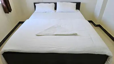 a bed with white sheets and a towel on it at Rodas Serviced Apartment in Coimbatore