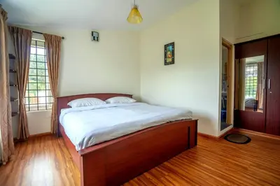 a bedroom with a bed with white sheets and wood floors at Greendale in Kotagiri