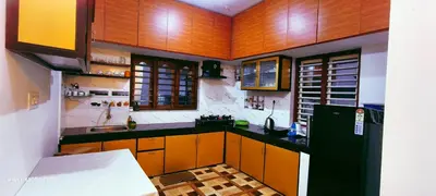 a kitchen with wooden cabinets and a black refrigerator at The Bulbul Nest Homestay in Gūdalūr