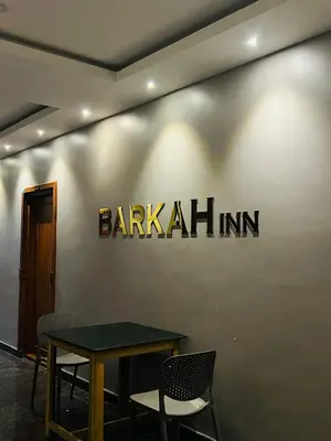 a table with chairs and a sign on a wall at Barkah inn in Kannur