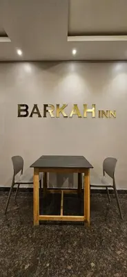 a table and chairs in front of a wall with a sign at Barkah inn in Kannur