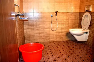a bathroom with a toilet and a red bucket at Club 7 Beach Resort in Kannur