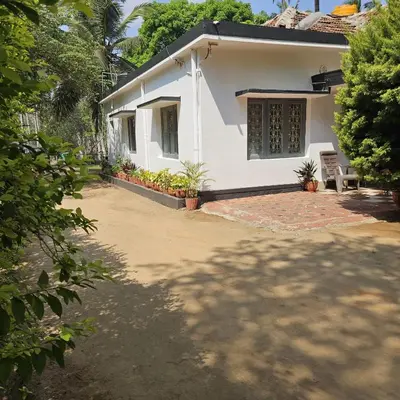 a white house with a chair in front of it at Mysticgreens Home Stay in Piriyāpatna
