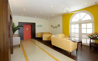 a living room with yellow furniture and an arched window at Hotel Luciya Palace in Trichūr