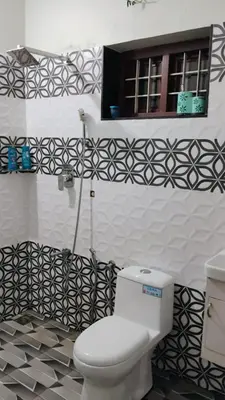 a bathroom with a white toilet and black and white tiles at Cozy Corner in Alwaye