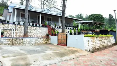 a house with a stone wall and a fence at Casa by the hills in Kotagiri