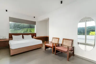 a bedroom with a bed and two chairs and a mirror at Finch,Kotagiri in Kotagiri