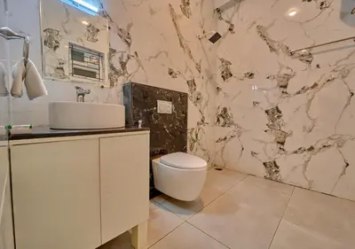 a bathroom with a white toilet and a marble wall at Central Homestay Ooty by VOYE HOMES Family-Friendly Budget Stay with Valley And Mountain Views in Ooty