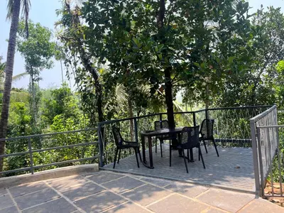a table and chairs on a deck with a tree at Pragathi Homestay in Mananthavady