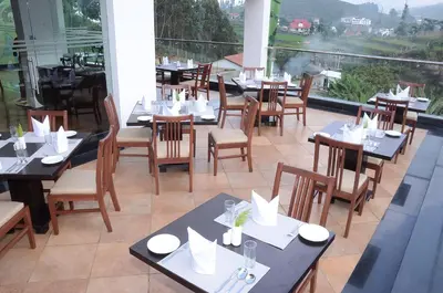 a restaurant with tables and chairs and a balcony at GReaT Trails Kodaikanal by GRT Hotels in Kodaikānāl