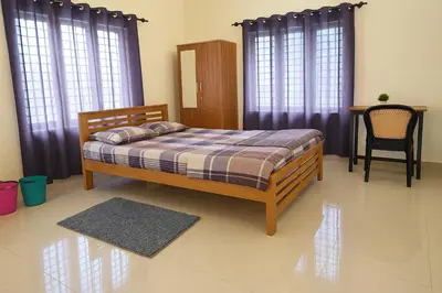 a bedroom with a bed and a chair and windows at Coffee View Holiday Homes in Thirunelli