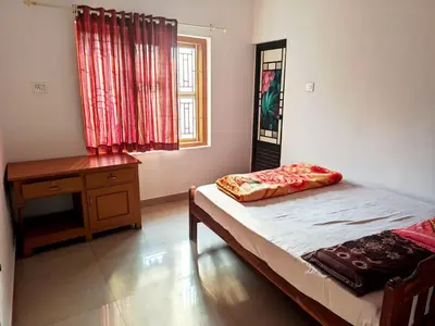 a bedroom with a bed and a desk and a window at Milu Homes in Thirunelli
