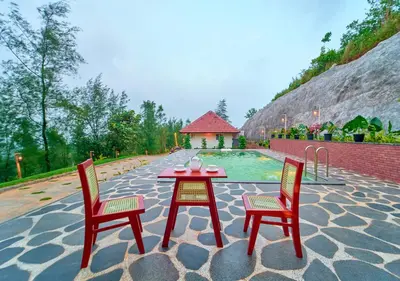 a table and two chairs on a patio with a pool at Whispering Hills Pine Malhar Pool & Tent Attappadi by VOYE HOMES in Attappādi