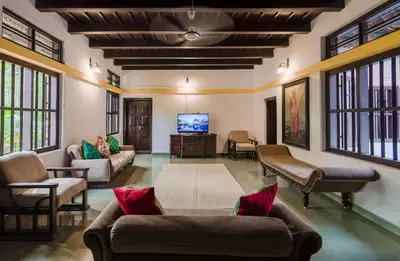 a living room with couches and a flat screen tv at SaffronStays Amaya - 5BR 300-year-old Kerala-style heritage villa with spa near Kannur Airport in Irikkūr