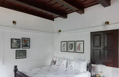 a bedroom with a bed with white sheets and pictures on the wall at SaffronStays Amaya - 5BR 300-year-old Kerala-style heritage villa with spa near Kannur Airport in Irikkūr